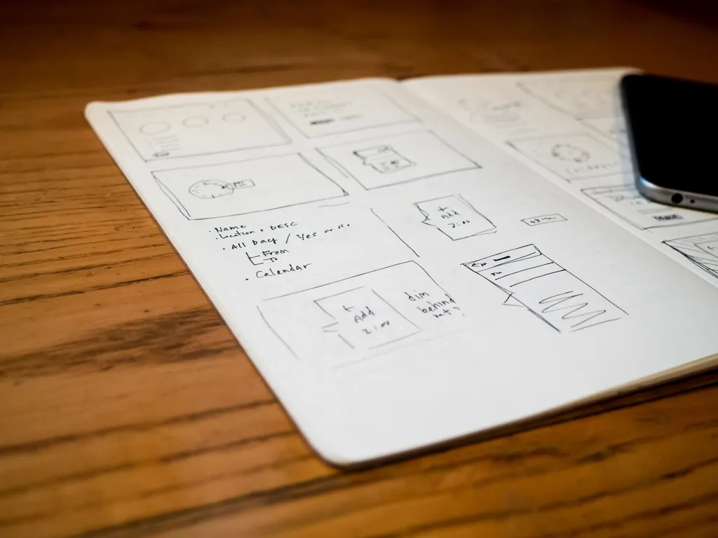 Hand-drawn sketches of mobile app screens in a notebook, with a phone next to it